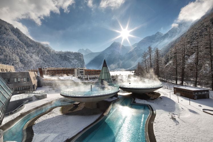 Winter landscape with a luxurious spa in the mountains, featuring steam rising from outdoor pools.